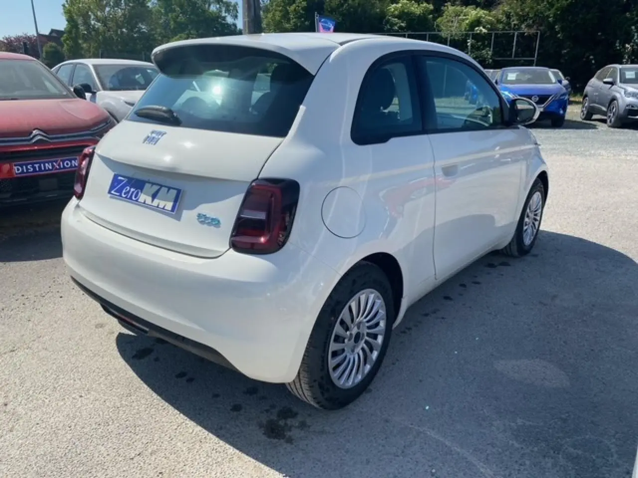 Vue 3/4 arrière droite d'une FIAT 500 électrique blanche métallisée, avec feux arrière foncés et jantes multibranches.