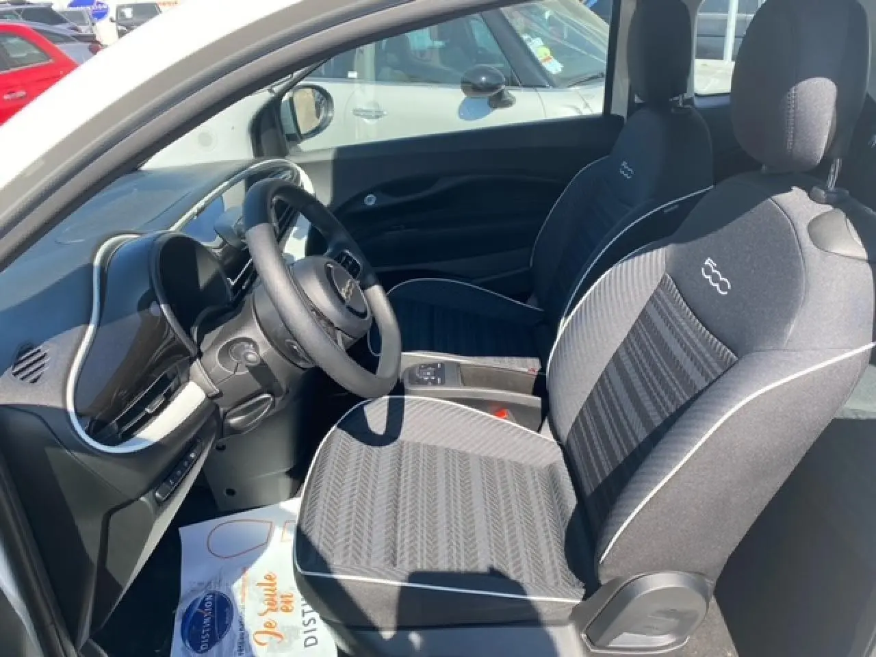 Vue intérieure côté conducteur de la Fiat 500 électrique blanche 2022, sièges noirs avec logo 500 brodé.