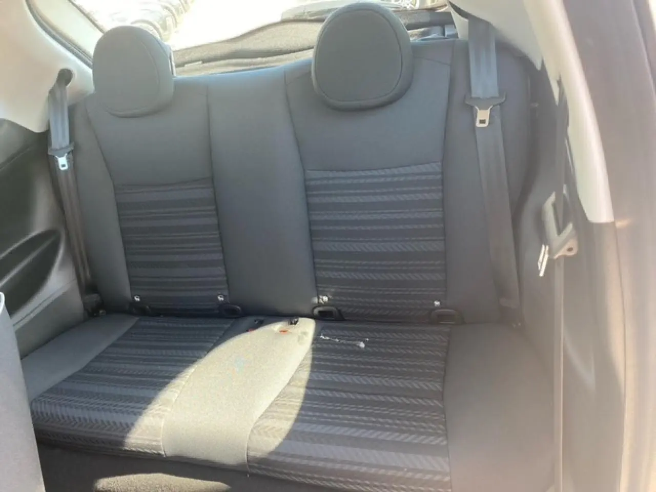 Vue intérieure sur la banquette arrière noire de la Fiat 500 électrique blanche, avec ceintures de sécurité visibles.