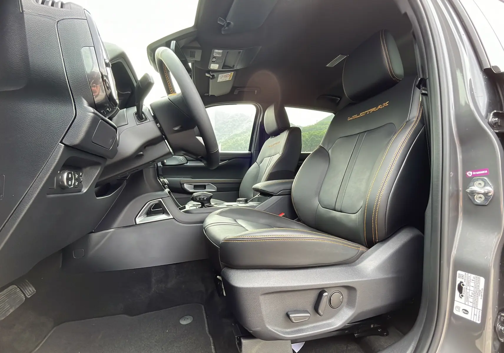 Vue intérieure côté conducteur du Ford Ranger Wildtrak gris carbone, sièges cuir noirs avec surpiqûres orange et logo Wildtrak brodé.