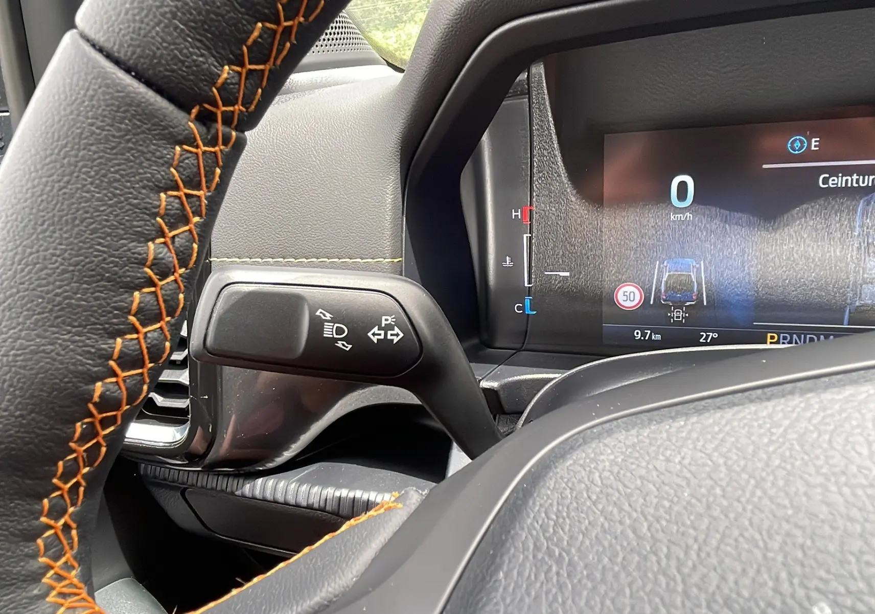 Gros plan sur le volant cuir noir avec surpiqûres orange et le combiné d'instruments numérique du Ford Ranger gris carbone.