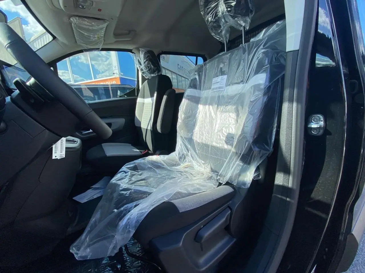 Vue intérieure côté conducteur du Citroën Berlingo noir 2026, siège avant protégé par une housse plastique.