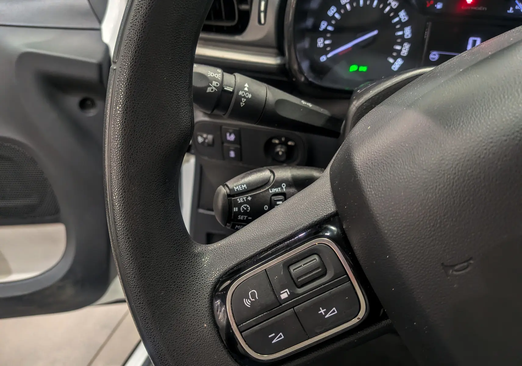 Gros plan sur le volant côté gauche d'une Citroën C3 Société blanc banquise, avec commandes audio intégrées visibles.