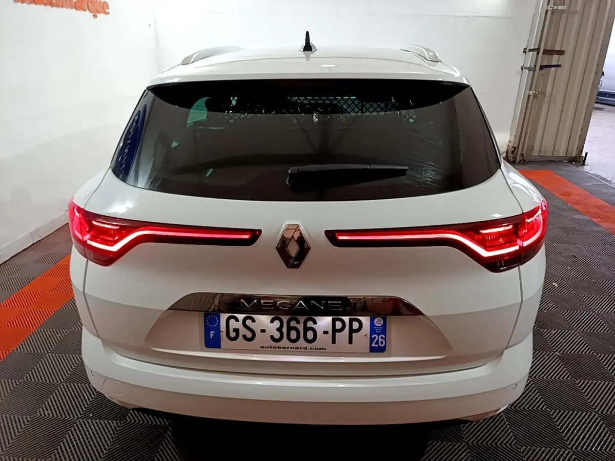 Vue arrière d'une Renault Mégane blanche 2023 avec feux LED allumés dans un garage.