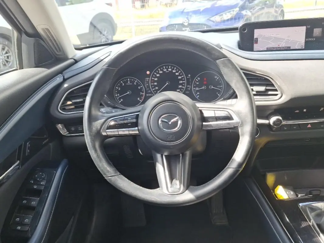 Vue intérieure centrée sur le volant noir multifonctions et le tableau de bord avec écran GPS du Mazda CX-30 gris 2020.