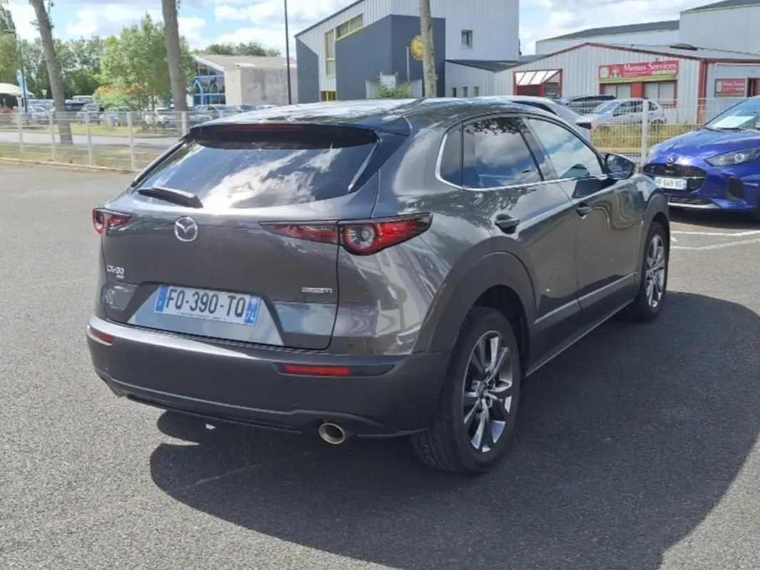 Vue 3/4 arrière droite d'un Mazda CX-30 gris 2020 avec vitres surteintées et jantes aluminium.