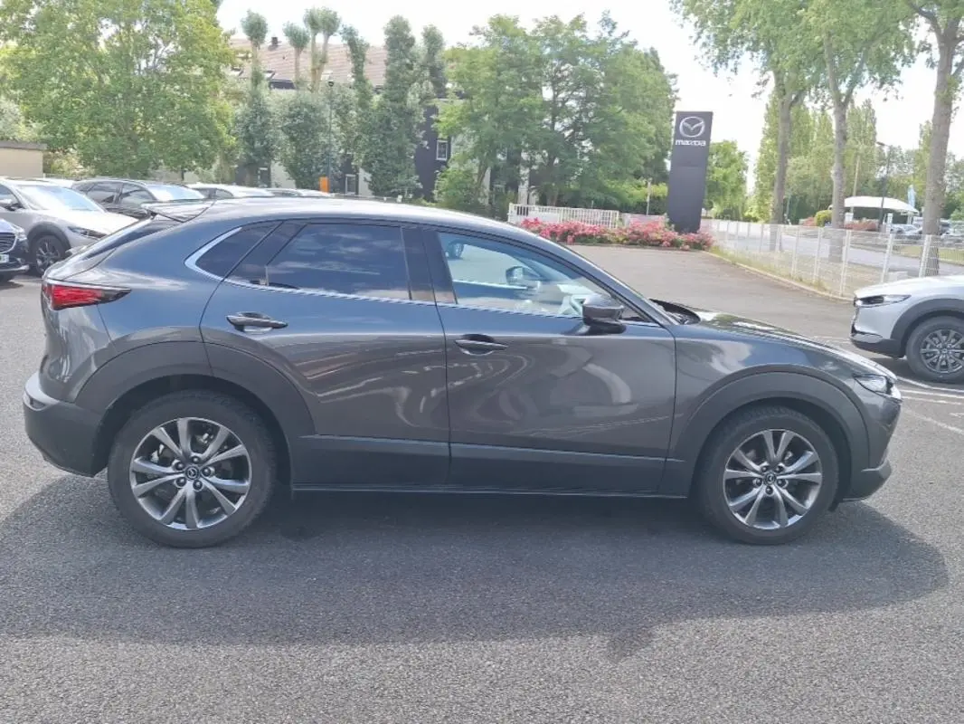 Vue de profil côté gauche d'un Mazda CX-30 gris avec vitres surteintées et jantes aluminium, stationné en extérieur.