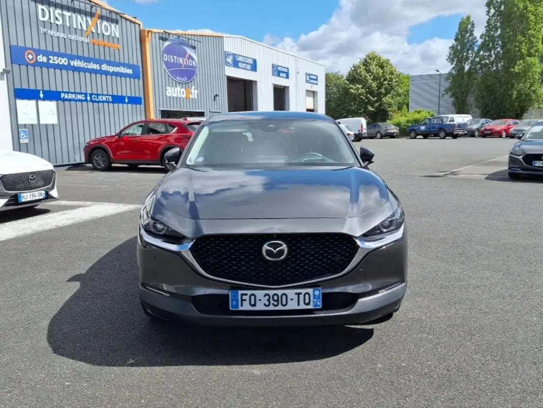 Vue de face d'un Mazda CX-30 gris 2020 avec calandre noire et phares effilés sur parking extérieur.