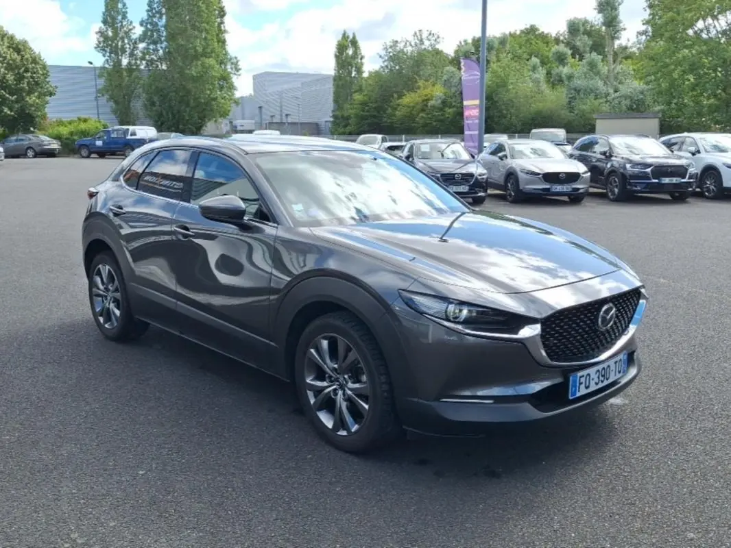 Vue 3/4 avant d'un Mazda CX-30 gris métallisé avec jantes aluminium, vitres surteintées et calandre noire ajourée.
