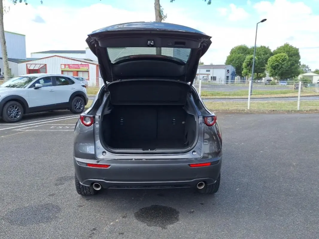 Vue arrière d'un Mazda CX-30 gris 2020 avec coffre ouvert, feux ronds et double sortie d'échappement visibles.
