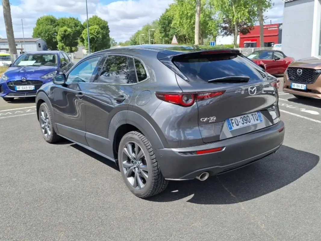 Vue 3/4 arrière droite d'un Mazda CX-30 gris avec vitres surteintées et jantes aluminium sur parking extérieur.