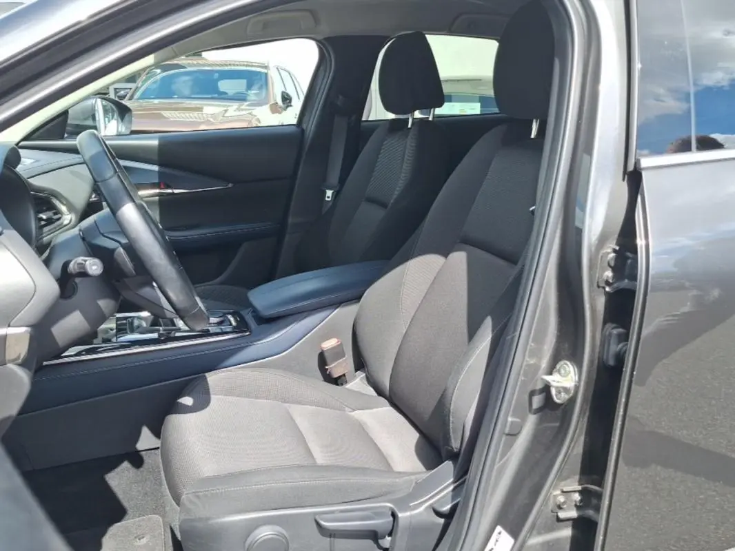 Intérieur avant droit du Mazda CX-30 gris 2020, sièges tissu noirs avec accoudoir central et volant multifonctions.