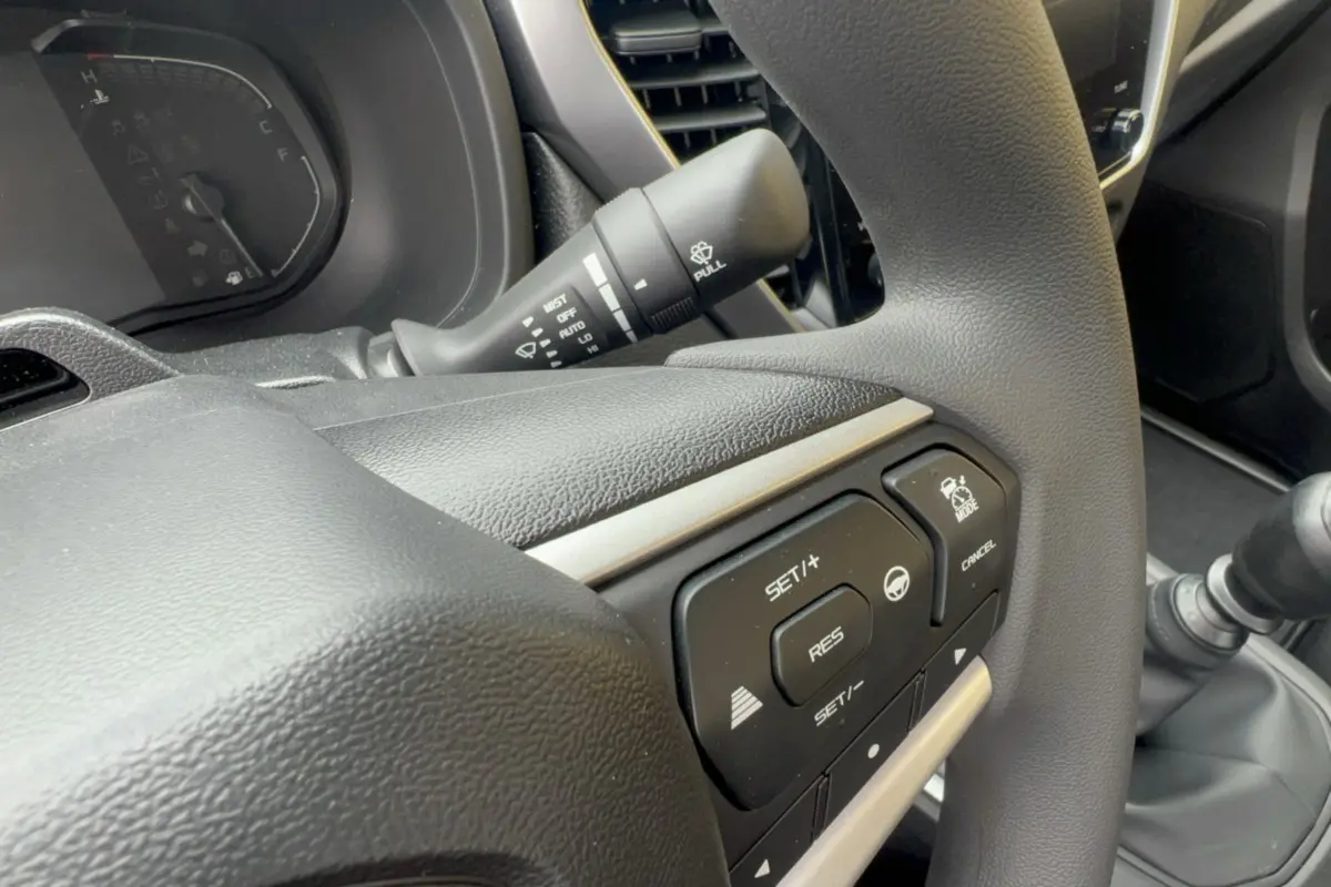 Gros plan sur le volant multifonctions noir de l'Isuzu D-MAX 2026 avec commandes de régulateur et boîte manuelle visible.