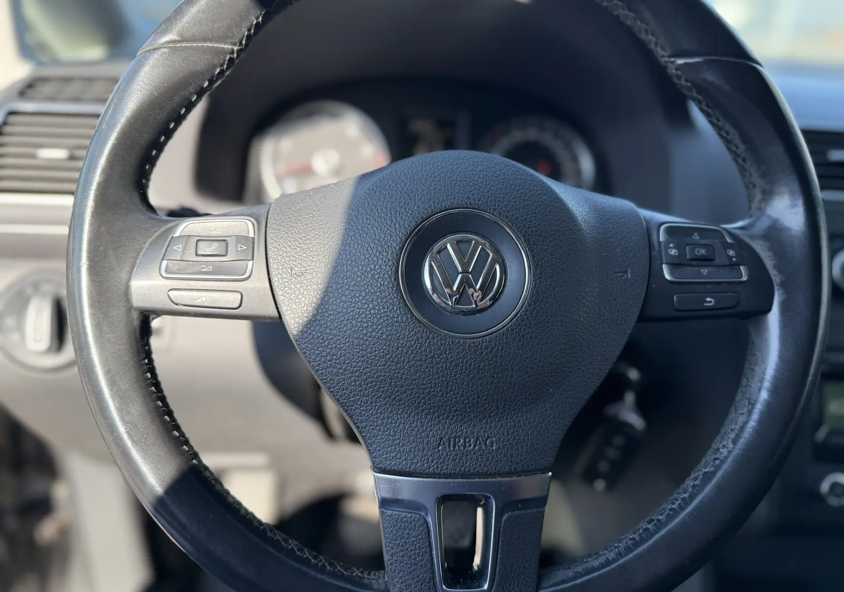 Gros plan sur le volant en cuir noir du Volkswagen Touran gris 2012, avec commandes intégrées visibles.
