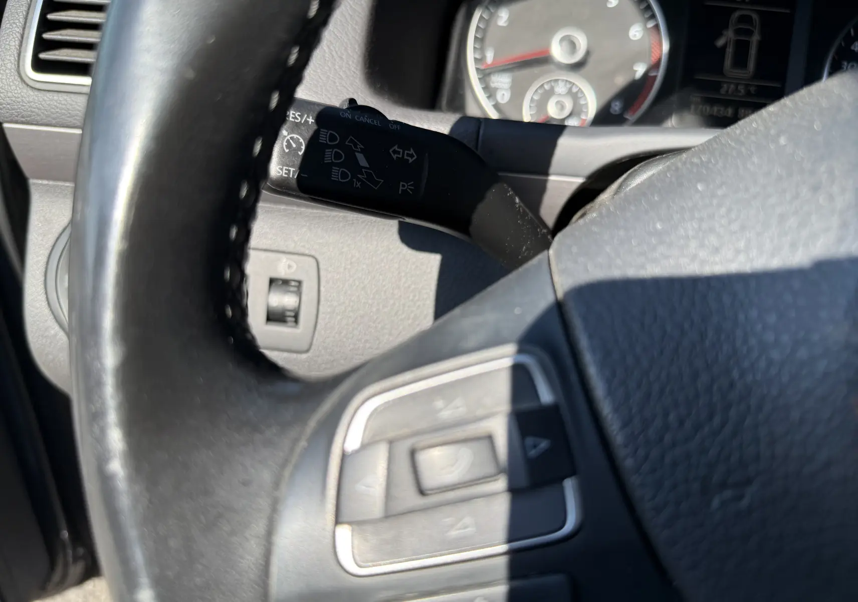 Gros plan sur le volant noir et le commodo gauche du tableau de bord du Volkswagen Touran gris, version 2012 essence.