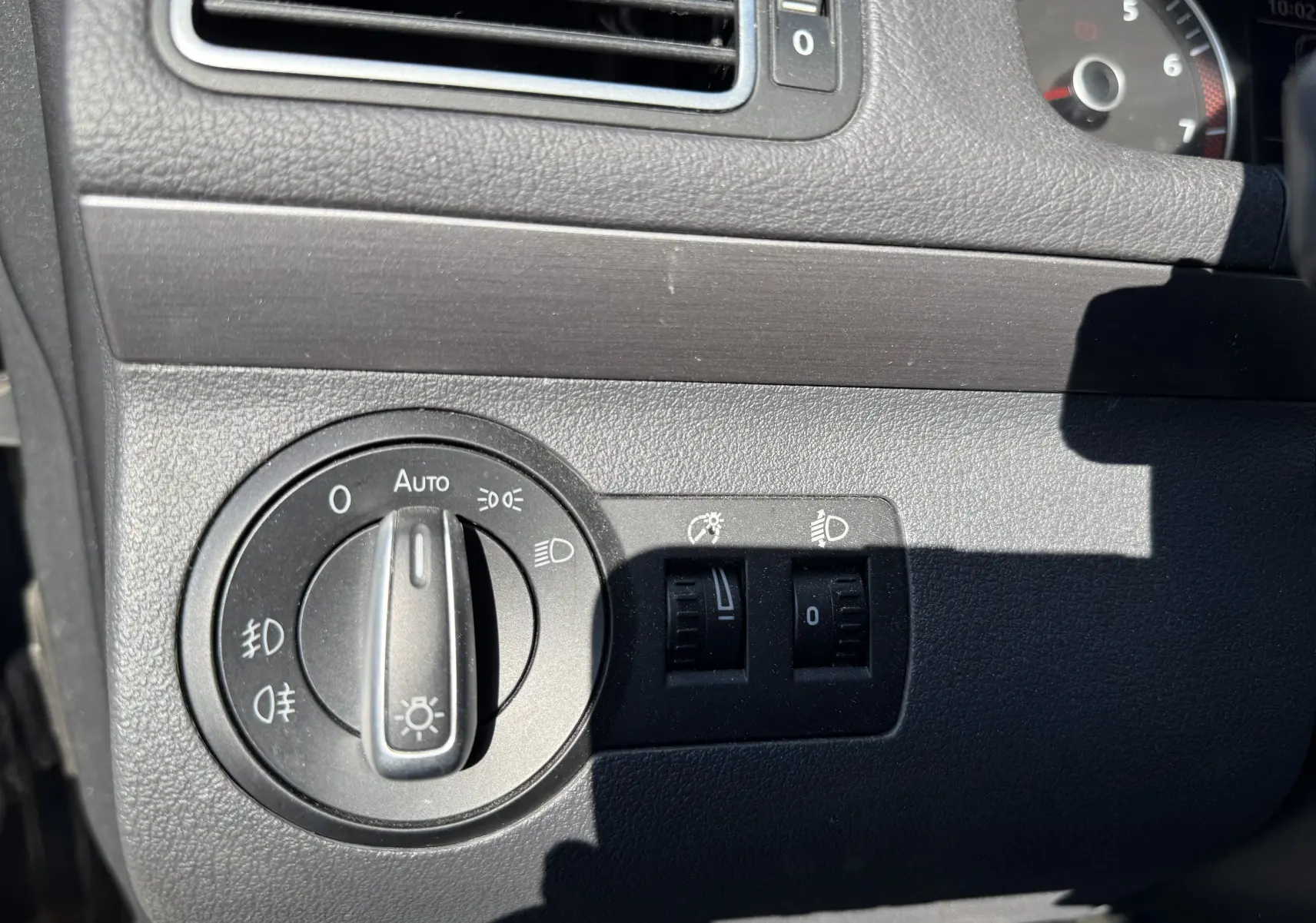 Gros plan sur le tableau de bord côté gauche du Volkswagen Touran gris 2012, montrant la commande des phares et réglages lumineux.