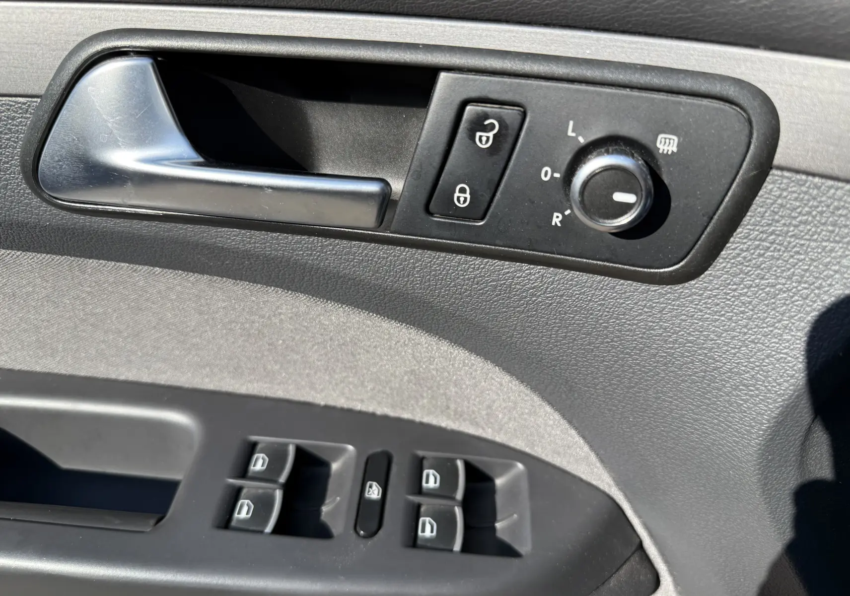 Gros plan sur la commande intérieure côté conducteur du Volkswagen Touran gris, avec poignée, réglage des rétroviseurs et boutons de vitres.
