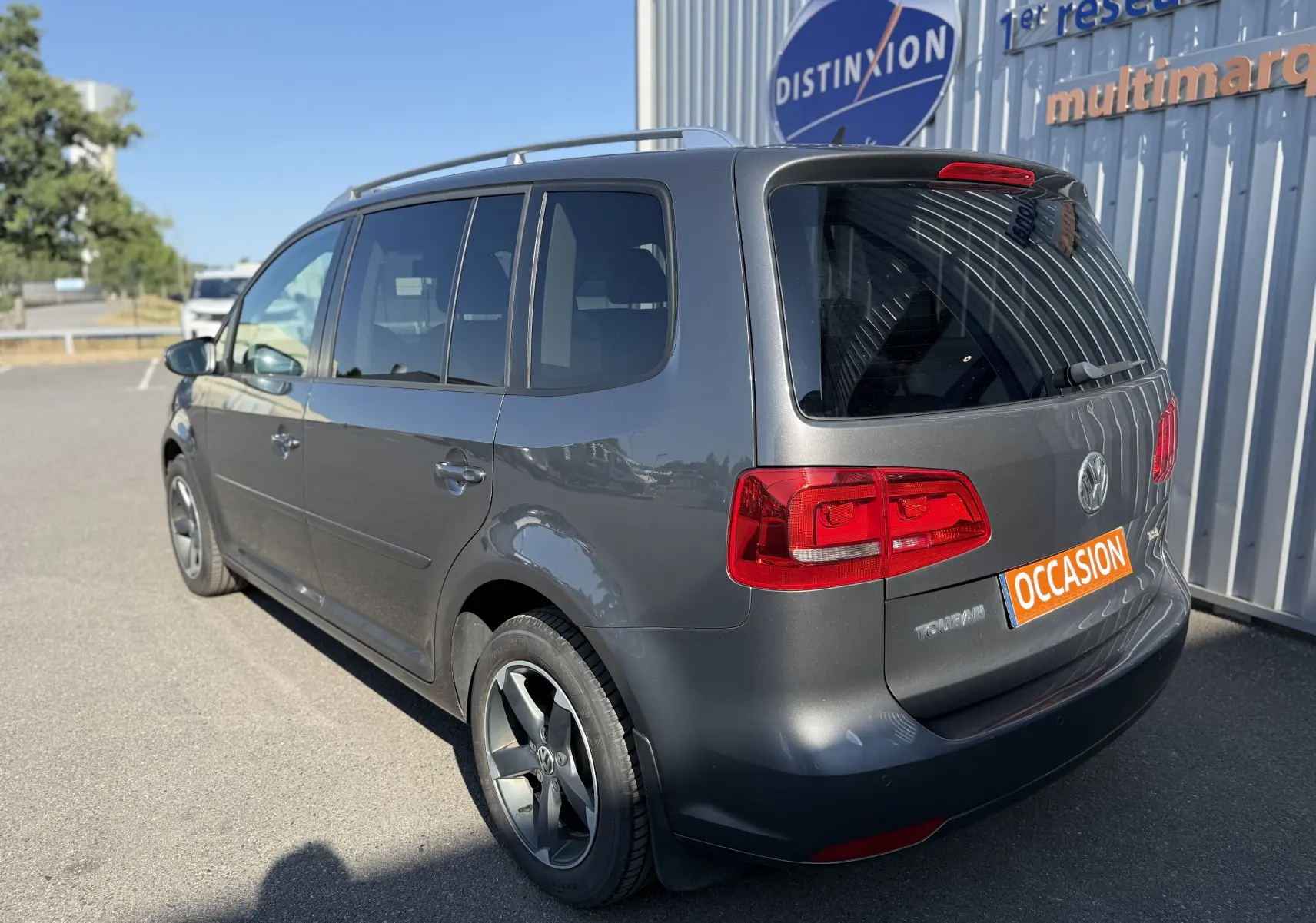 Volkswagen Touran gris 2012 en 3/4 arrière droit, avec jantes alliage et plaque "OCCASION" visible.