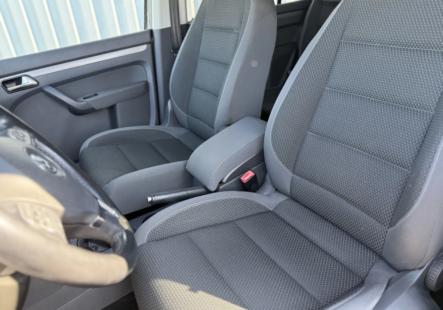 Vue intérieure rapprochée des sièges avant en tissu gris du Volkswagen Touran 1.4 TSI 7 places, avec accoudoir central.