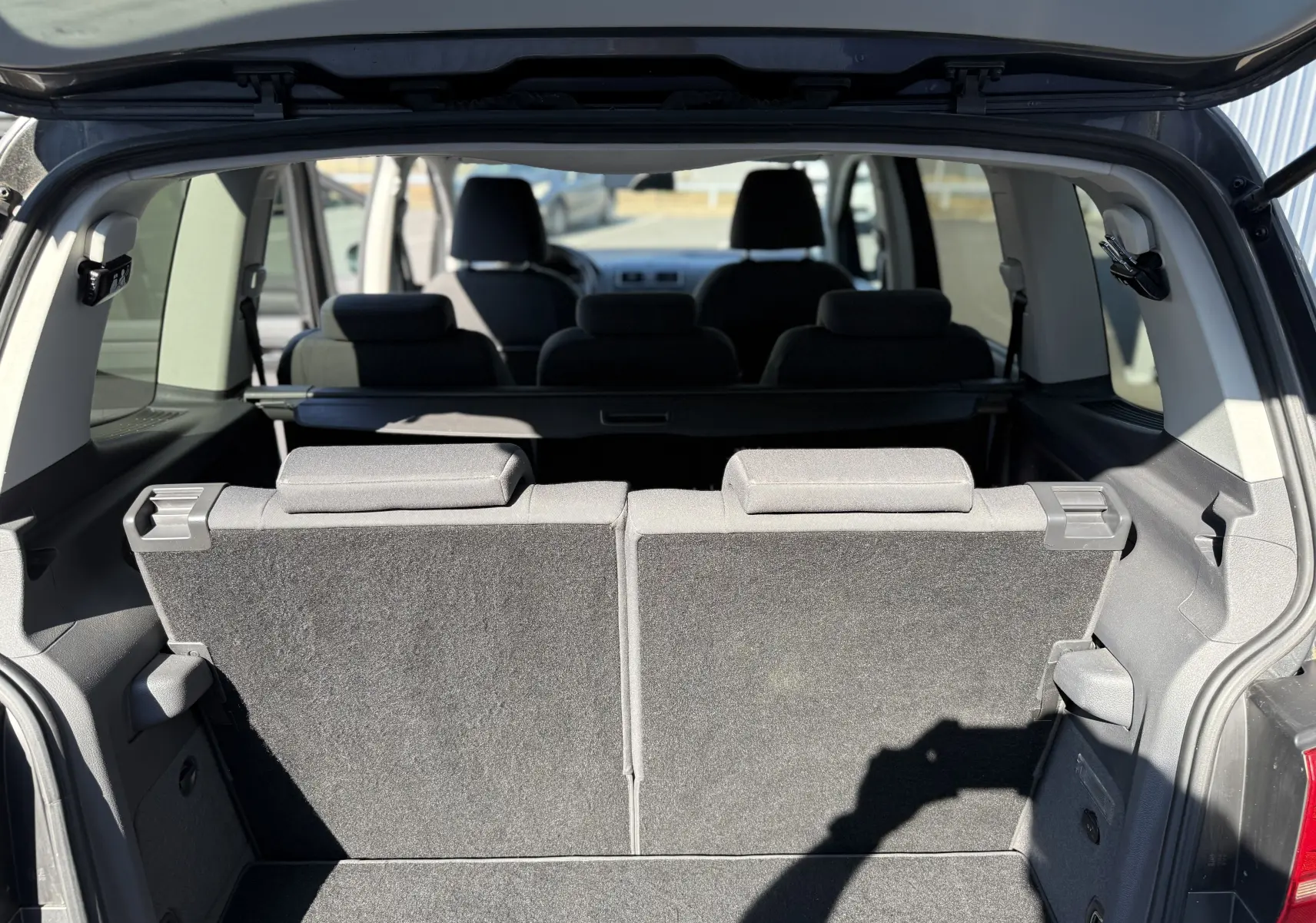 Vue arrière du coffre ouvert d’un Volkswagen Touran gris 2012, montrant la troisième rangée de sièges relevée en tissu noir.