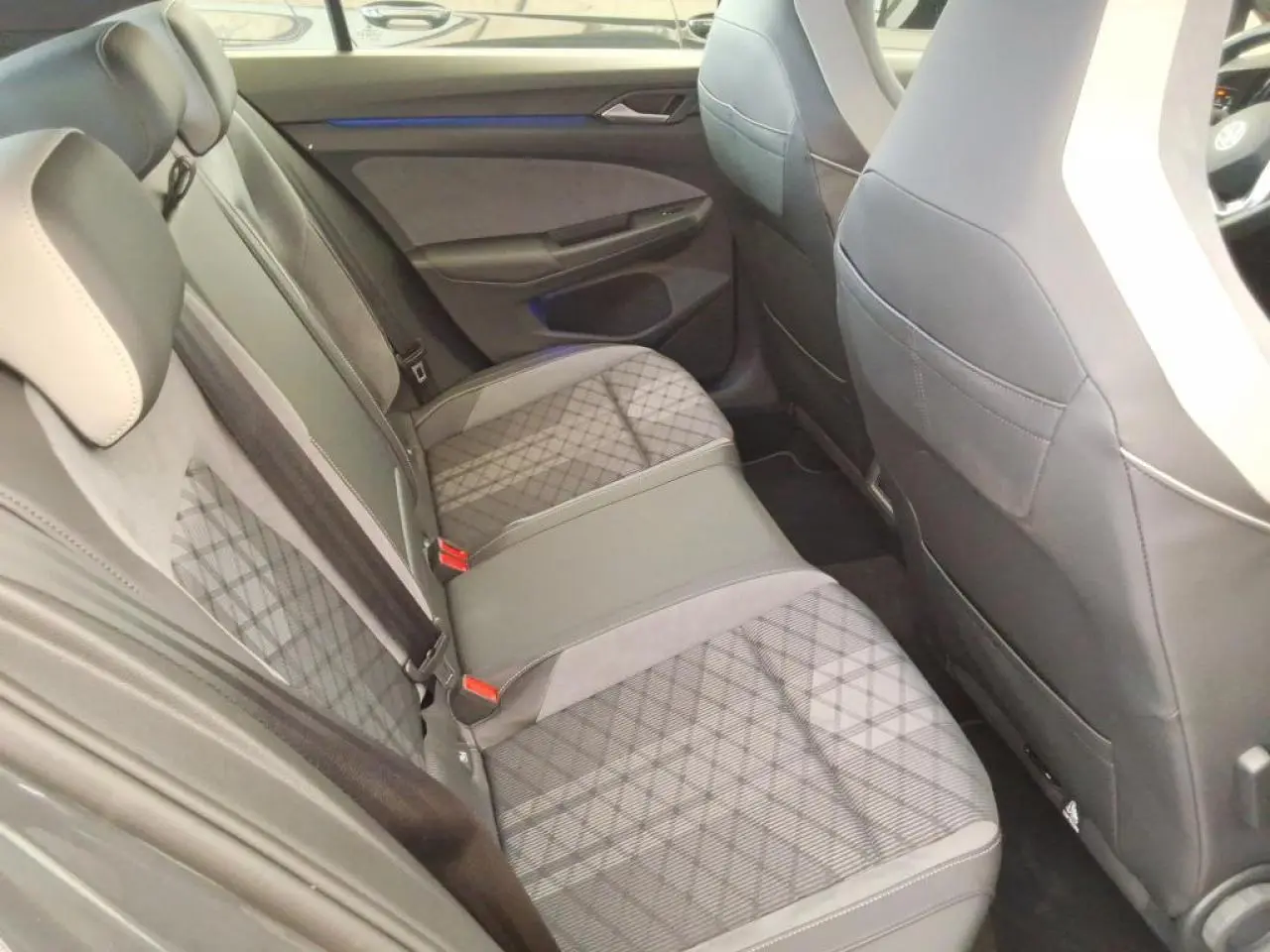Vue intérieure arrière côté gauche de la Volkswagen Golf 2024 avec sellerie tissu gris à motifs et appuis-tête intégrés.