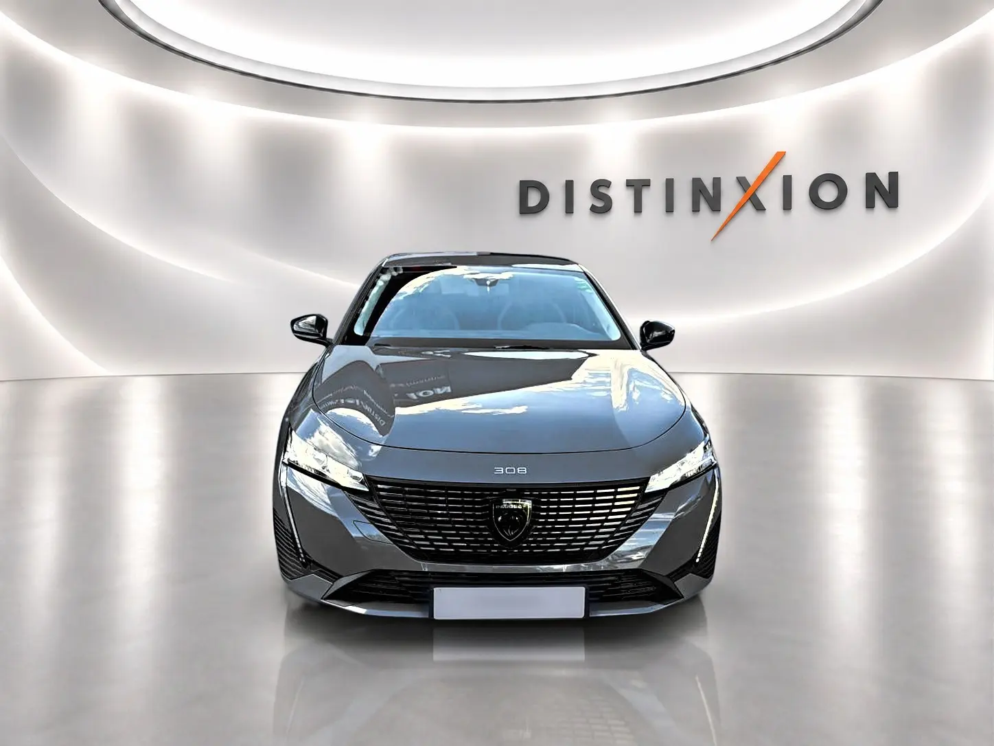 Vue frontale d'une Peugeot 308 gris selenium 2025, avec calandre noire et phares LED fins dans un showroom lumineux.