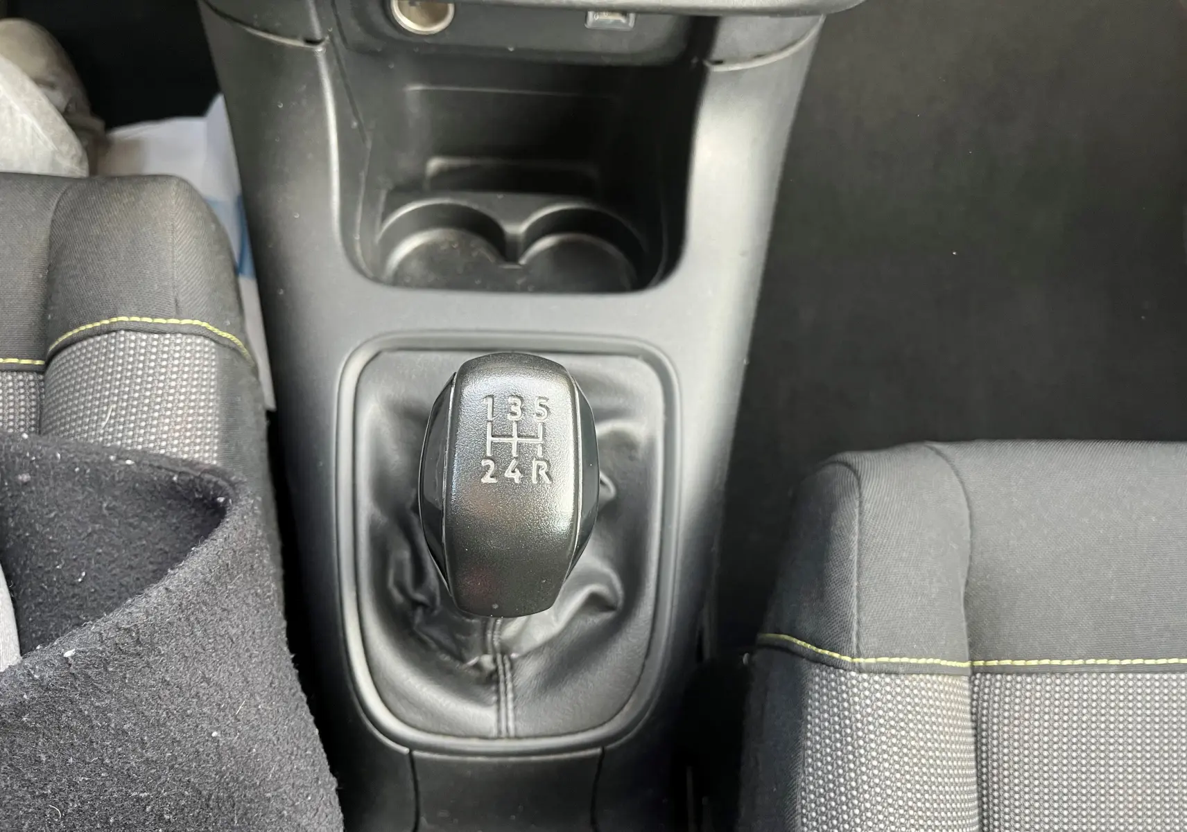 Le levier de vitesses manuel noir vu de dessus dans l'habitacle d'une Citroën C3 blanche de 2019, avec sièges gris et surpiqûres jaunes.