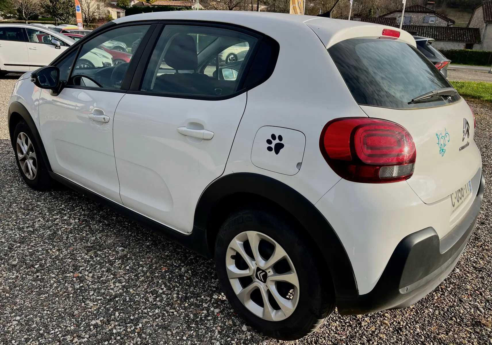 Vue 3/4 arrière droite d'une Citroën C3 blanche 2019 avec autocollant patte de chien sur la trappe à carburant.