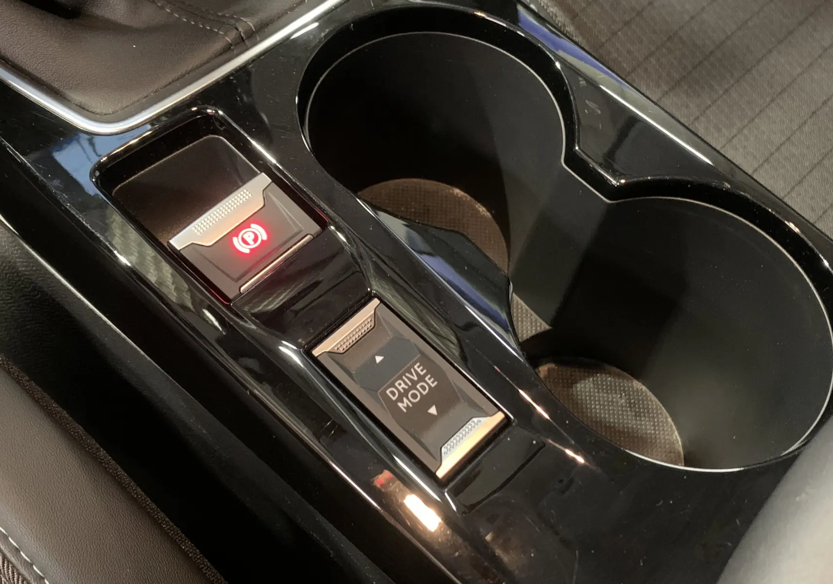 Gros plan sur la console centrale noire de la Peugeot 208 gris, avec bouton frein à main électronique et mode de conduite.