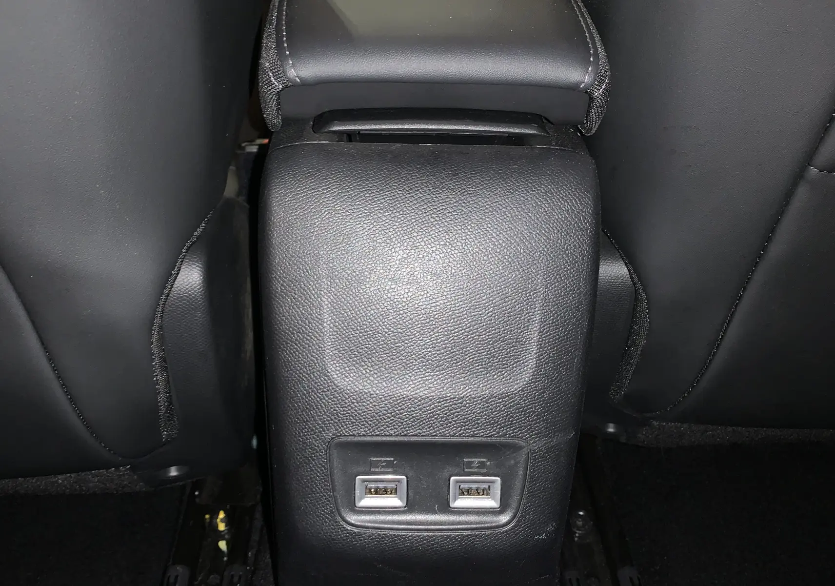 Vue rapprochée de la console arrière noire avec deux ports USB entre les sièges avant d’une Peugeot 208 gris.