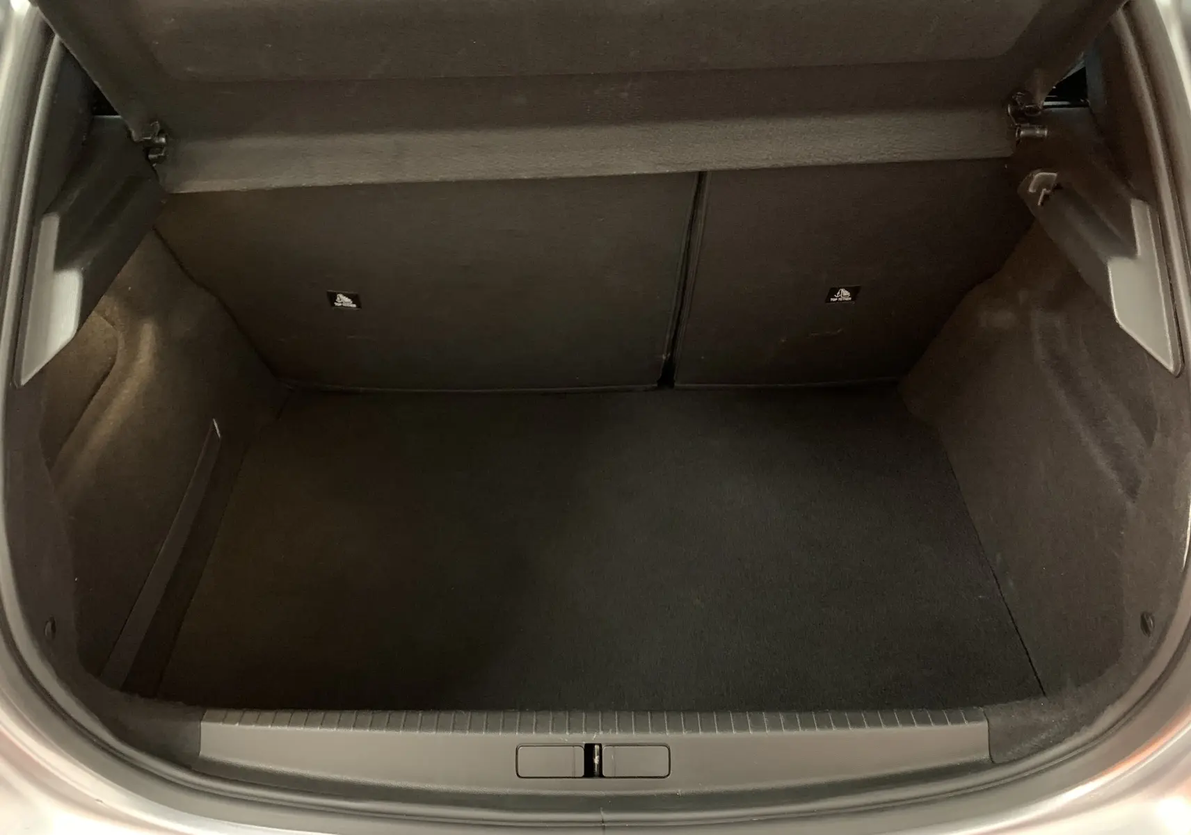 Coffre ouvert de la Peugeot 208 PureTech 100 Allure Business gris, vue plongeante montrant l’espace de rangement vide.