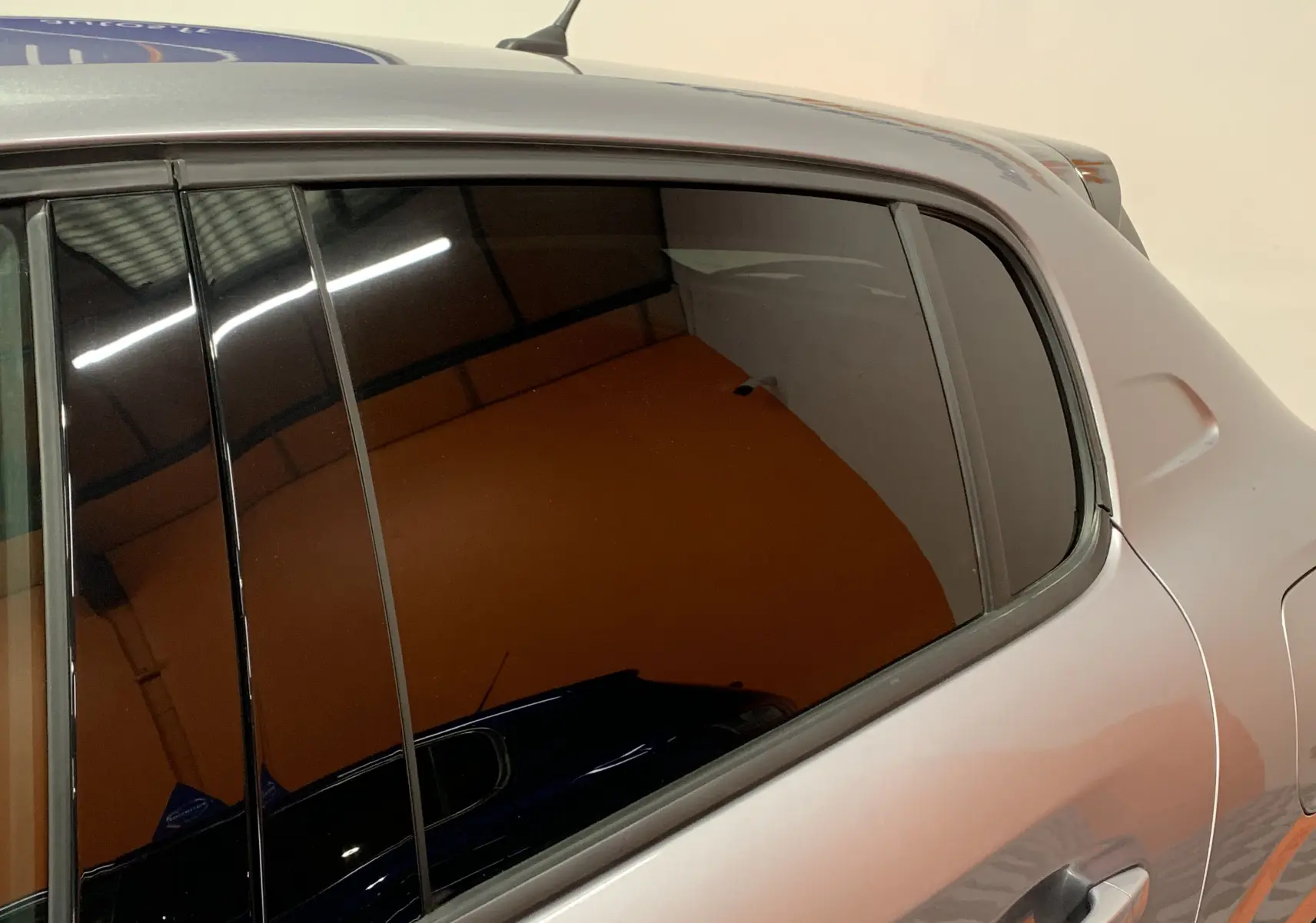 Vue rapprochée du côté gauche arrière d'une Peugeot 208 PureTech 100 Allure Business gris avec vitre teintée.