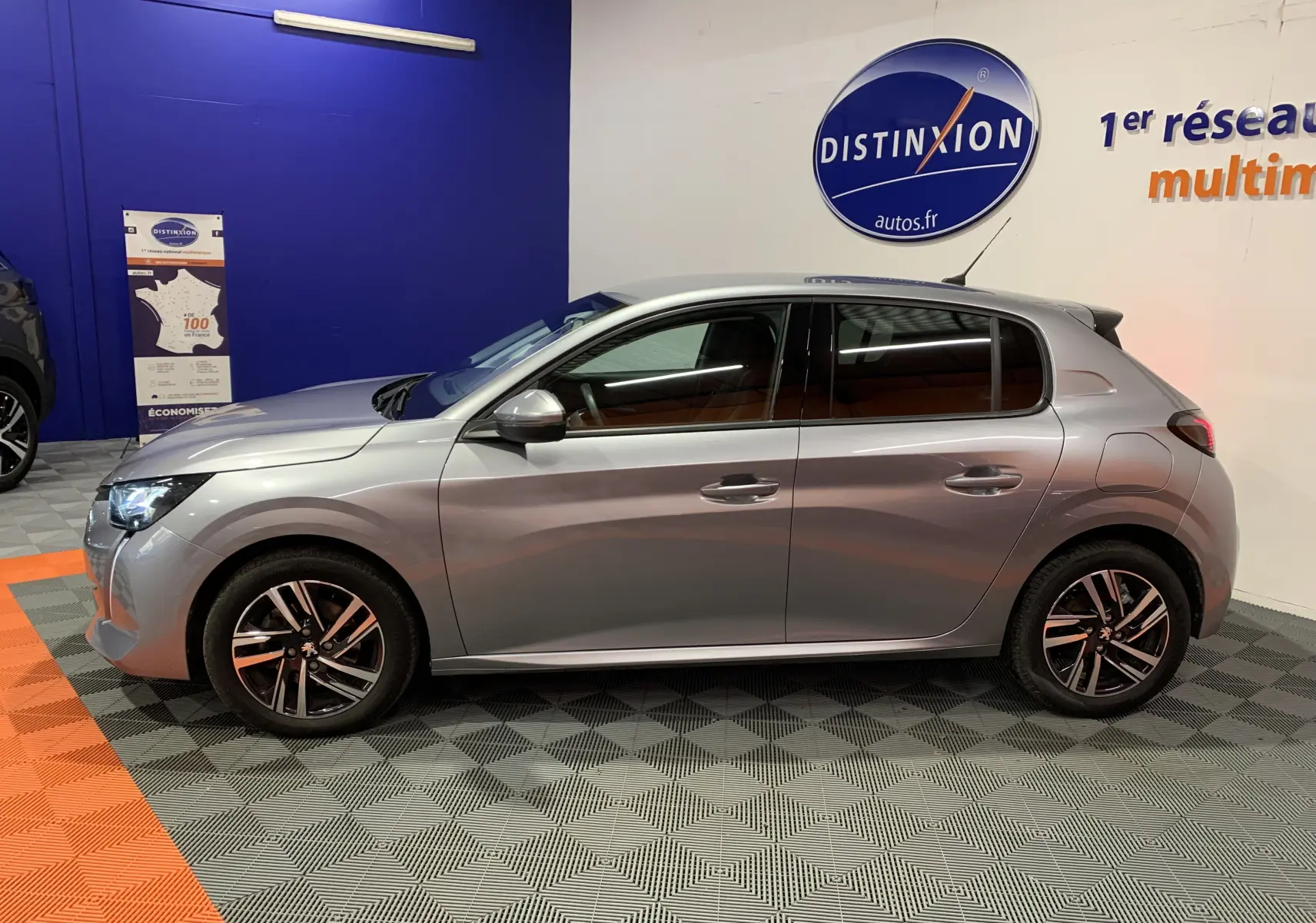 Profil droit d'une Peugeot 208 gris métallisé de 2021, finition Allure Business avec jantes alliage et phares LED allumés.