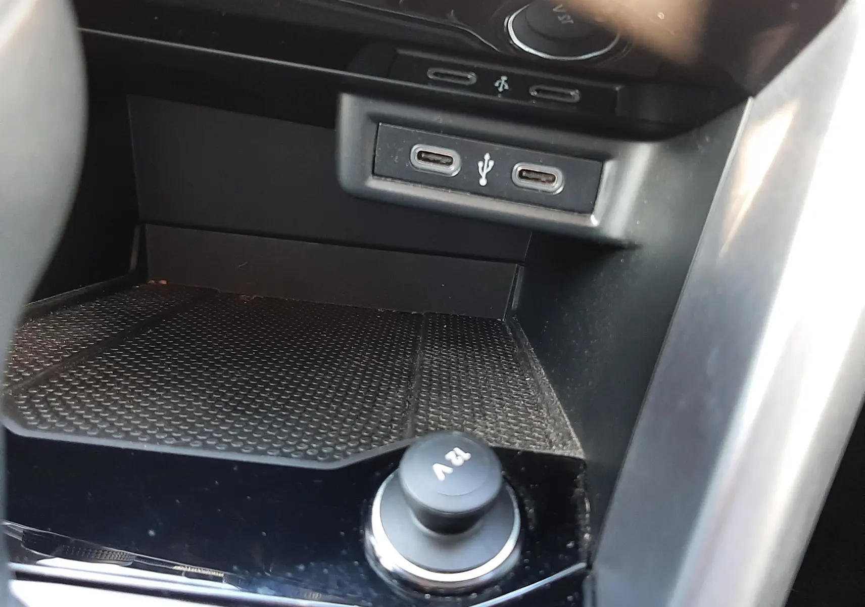 Vue rapprochée de la console centrale du Volkswagen T-Roc 2022, montrant prises USB et prise 12V sur fond noir brillant.