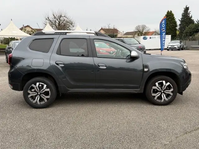 Vue latérale droite d'un Dacia Duster 1.5 BlueDCI 115 Prestige+ gris comète avec jantes alliage distinctives en extérieur.
