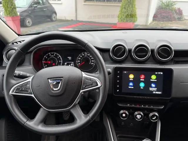 Vue intérieure centrée sur le volant noir du Dacia Duster 2022, avec tableau de bord et écran tactile multimédia allumé.