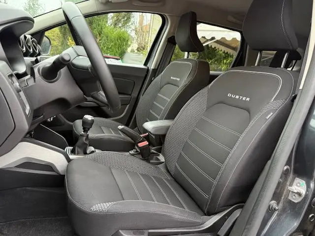 Vue intérieure côté gauche du Dacia Duster 2022 gris comète, sièges avant noirs avec logo Duster brodé.