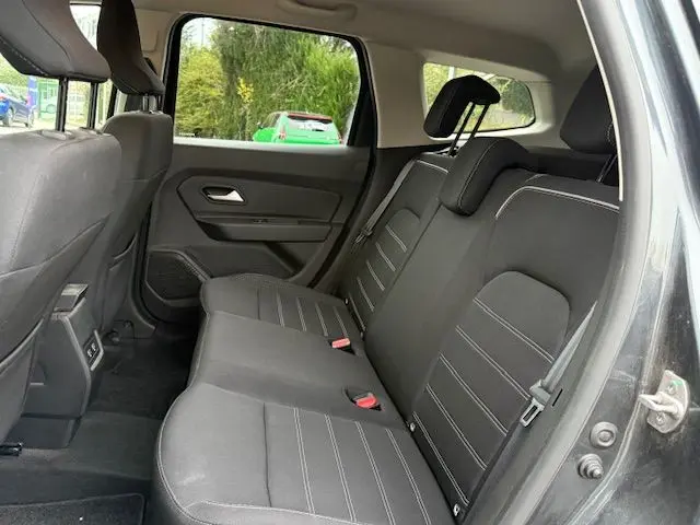Vue intérieure arrière droite du Dacia Duster 2022 gris comète, montrant les sièges arrière en tissu avec surpiqûres blanches.