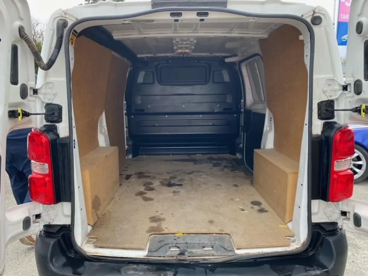 Vue arrière ouverte du Citroën Jumpy blanc 2019 montrant l’intérieur utilitaire avec habillage bois et plancher usé.