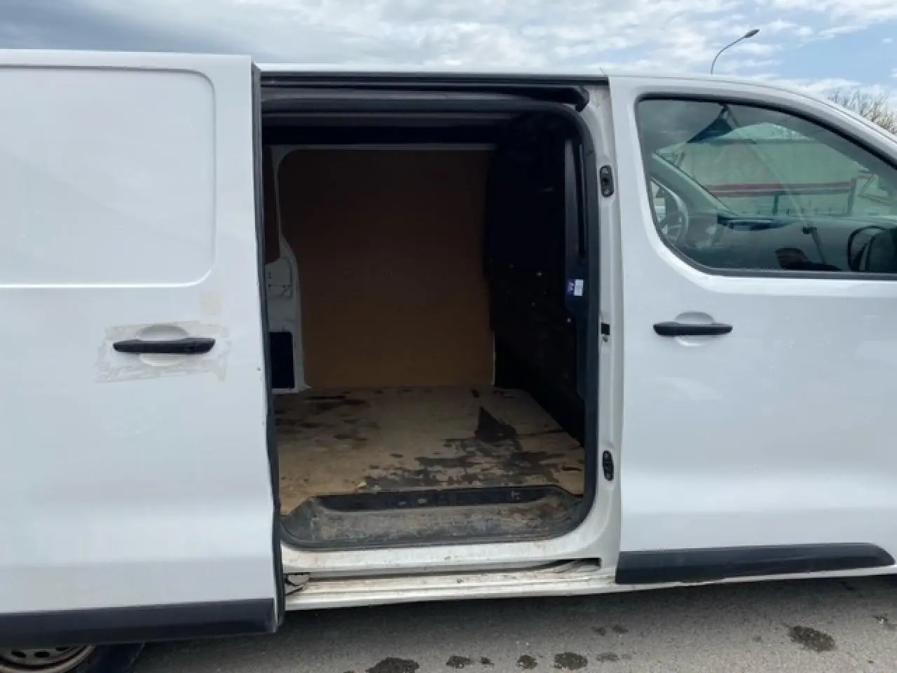 Vue latérale gauche d’un Citroën Jumpy blanc avec porte coulissante ouverte montrant l’intérieur utilitaire en bois.