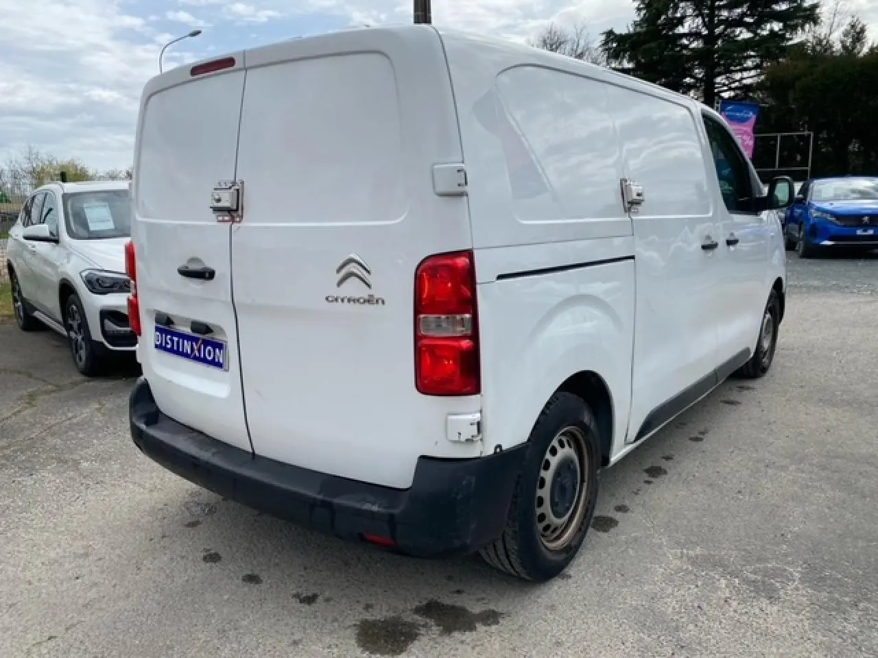 Vue 3/4 arrière droite d’un utilitaire Citroën Jumpy blanc, portes arrière battantes et porte latérale coulissante visibles.