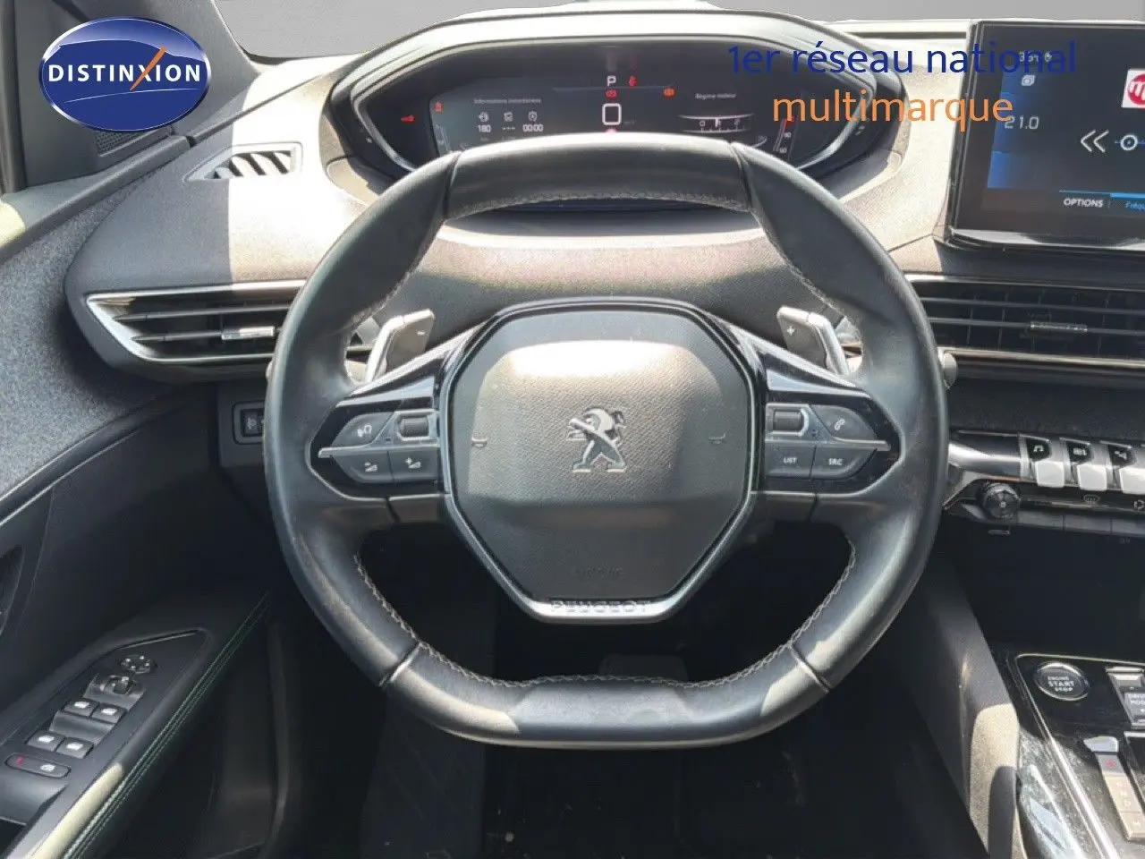 Vue intérieure centrée sur le volant cuir noir du Peugeot 5008 2023 avec tableau de bord digital et commandes intégrées.