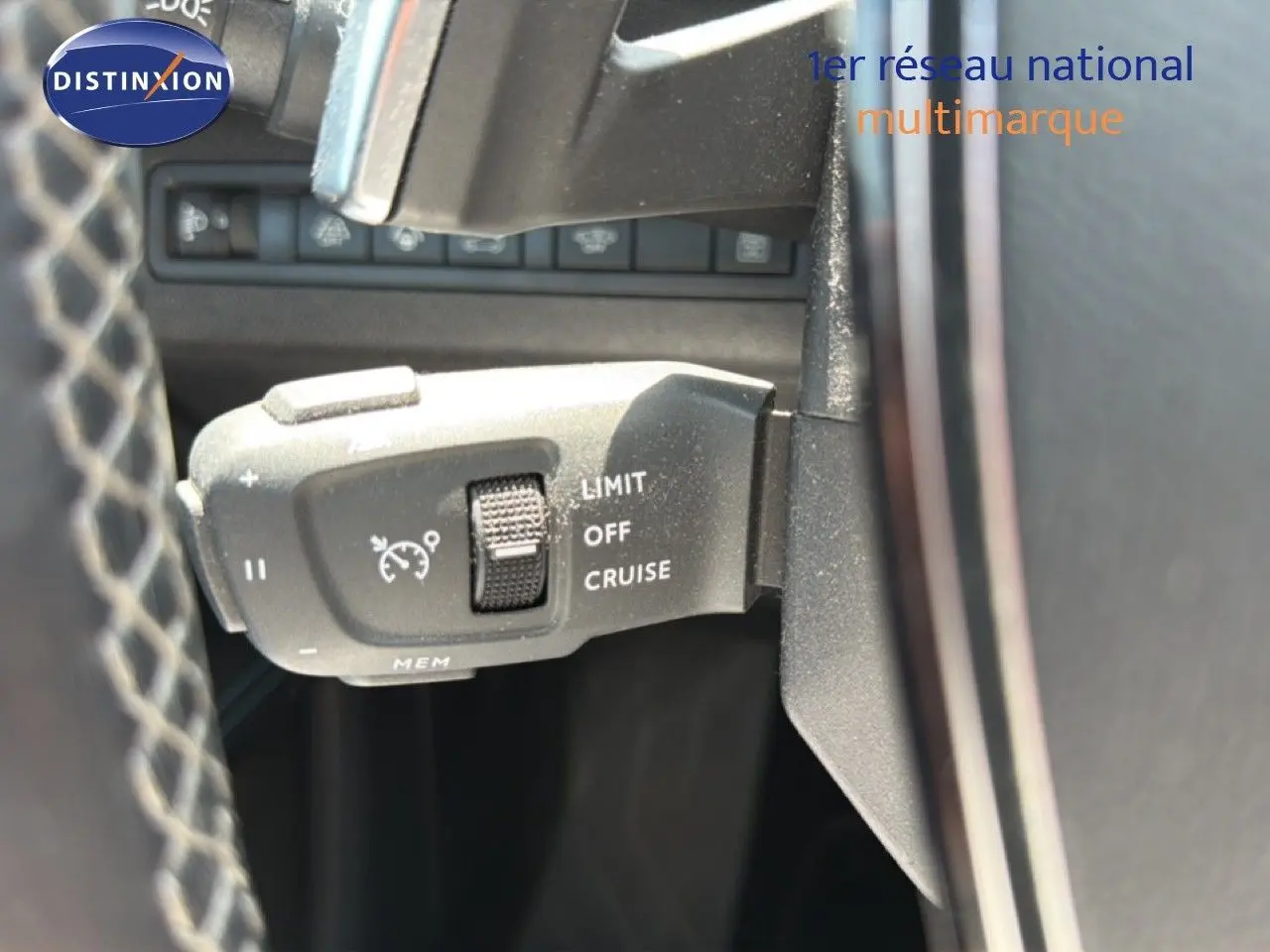 Gros plan sur la commande de régulateur de vitesse à gauche du volant dans un Peugeot 5008 gris Platinium 2023.