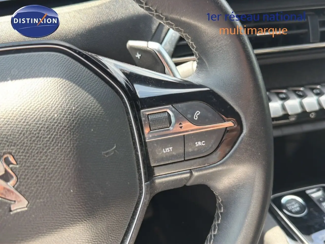 Gros plan sur le volant en cuir noir du Peugeot 5008 2023, avec commandes intégrées et palettes au volant visibles.