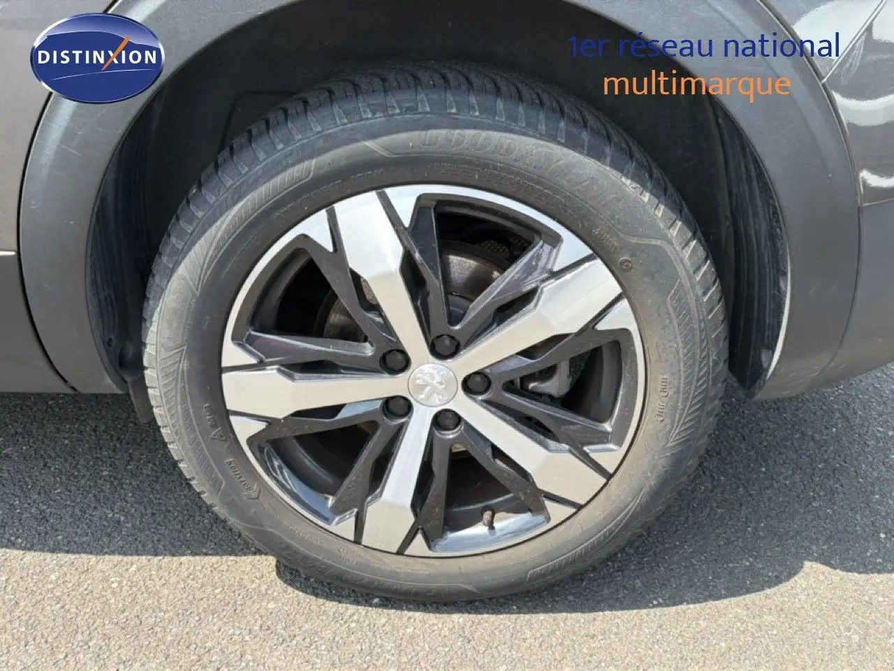 Gros plan sur la roue avant droite du Peugeot 5008 gris Platinium avec jante alliage bicolore et logo lion central.