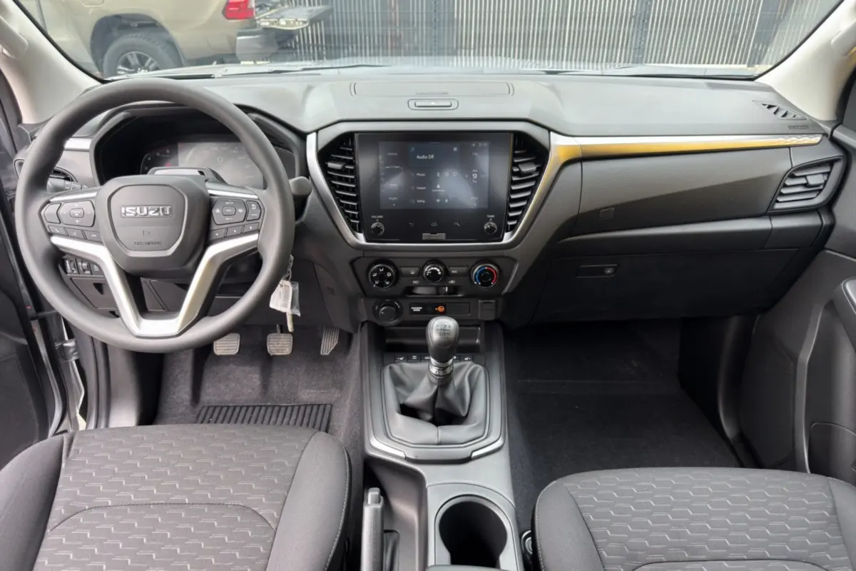 Vue intérieure avant de l'Isuzu D-MAX 2026, tableau de bord noir avec écran tactile et levier de vitesses manuel.