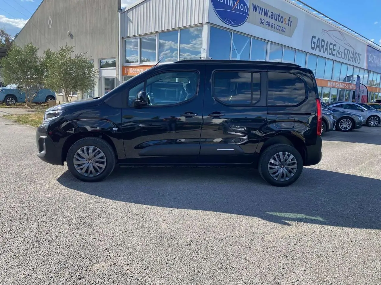 Profil côté gauche du Citroën Berlingo noir 2026, avec portes coulissantes et vitres surteintées, stationné devant un garage.