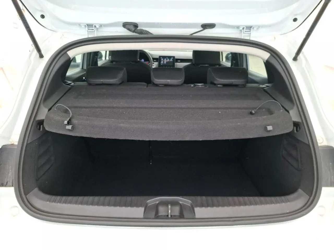 Vue arrière du coffre ouvert d'une Renault Clio blanche 2024 avec plage arrière noire et sièges arrière visibles.