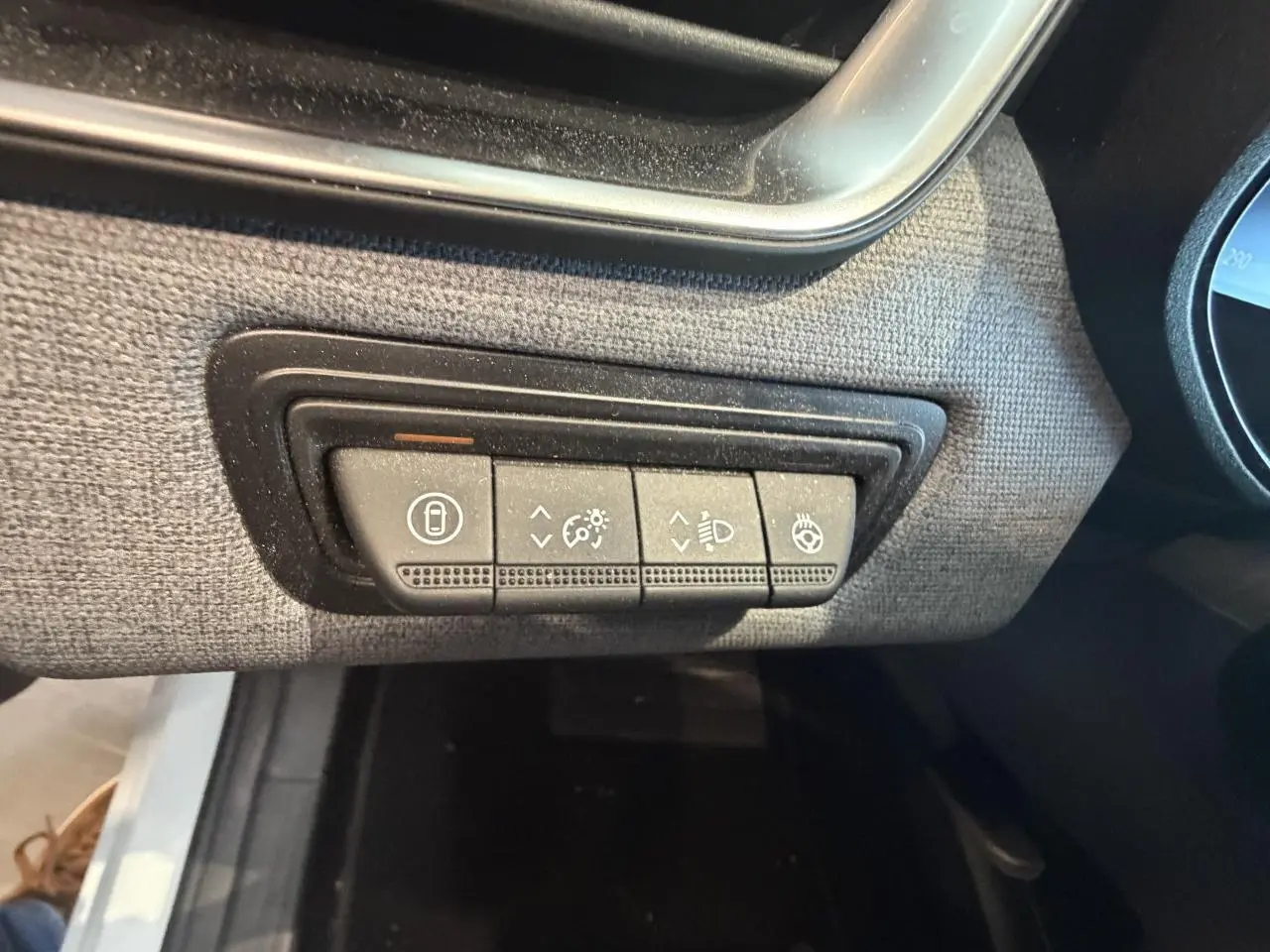 Gros plan sur les commandes d’éclairage et de verrouillage sur la planche de bord tissu gris de la Renault Clio blanche.
