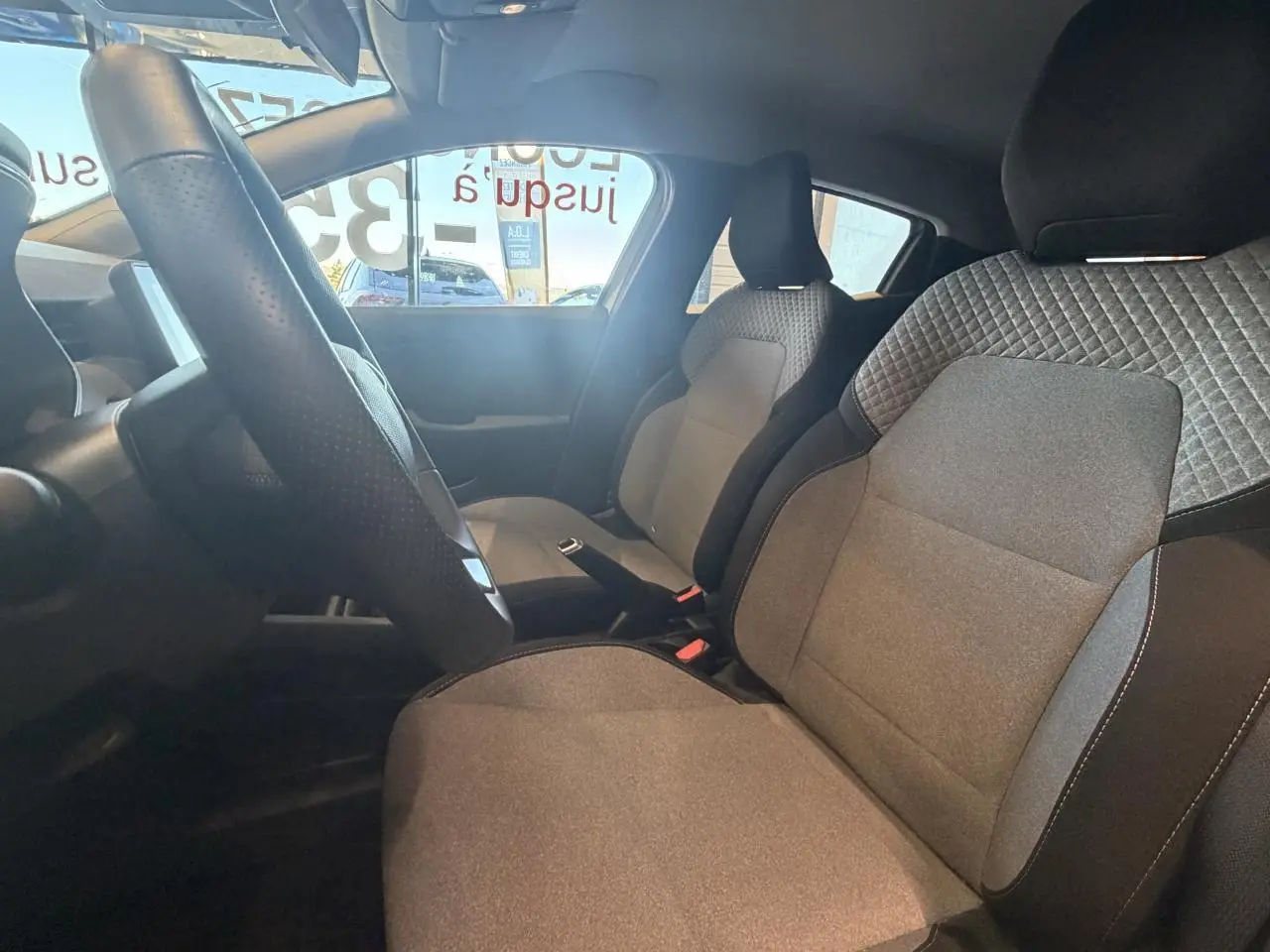 Intérieur de la Renault Clio 2024 vu côté droit, sièges tissu gris avec motifs 3D et volant multifonction noir.